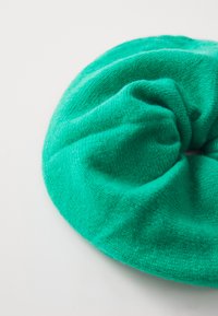 Scrunchie verde tricotat, cu o textură moale, formă rotundă și design strâns, având o culoare uniformă și o strălucire subtilă.