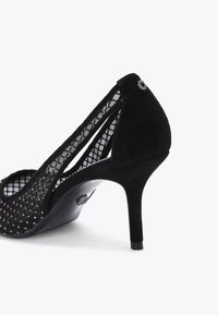 Escarpin en suède noir avec un design en dentelle, bout pointu et un accent décoratif à l'arrière, sur un talon aiguille fin.