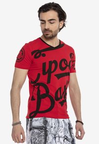 Rotes kurzärmliges T-Shirt mit schwarzer Graffiti-Schrift, V-Ausschnitt-Design und einem runden Logo auf dem linken Ärmel. Baumwollstoff.