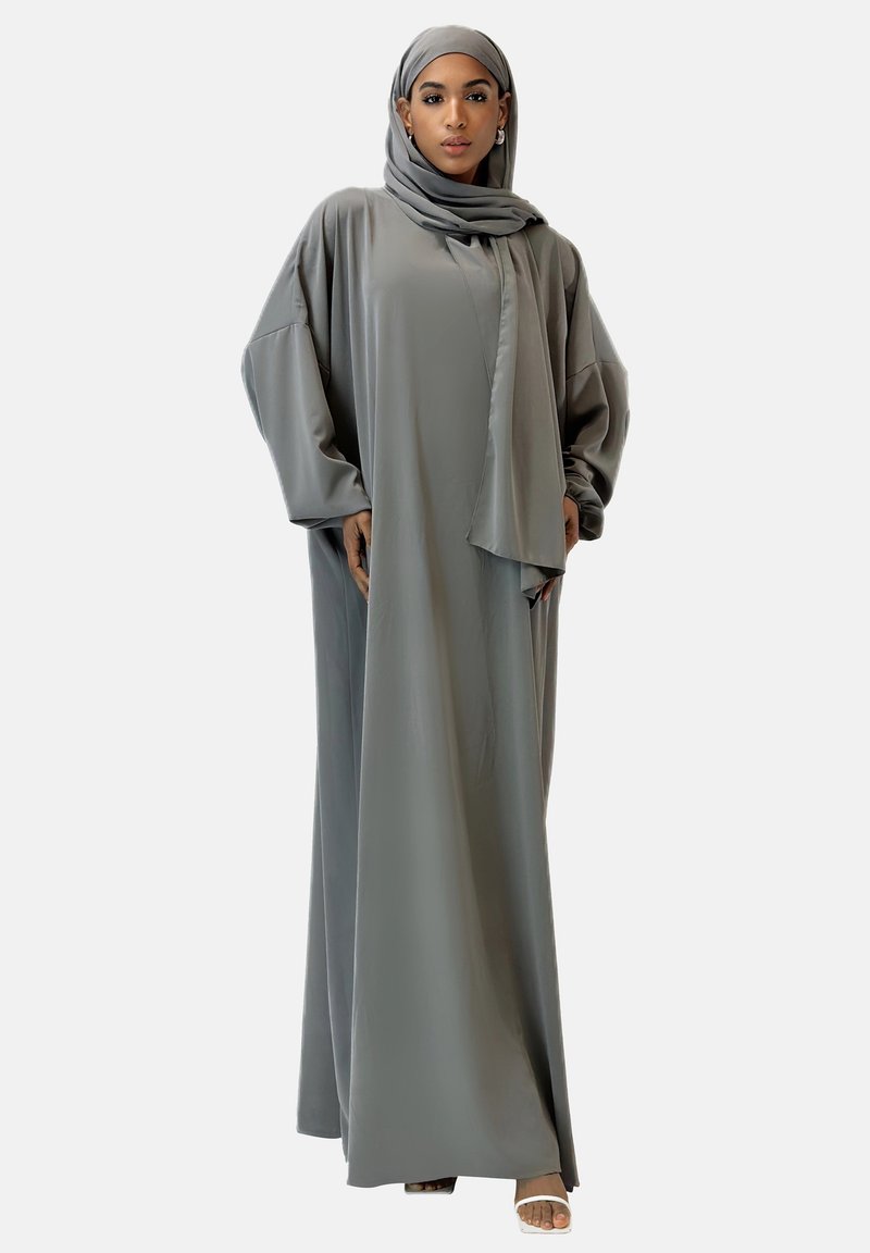 Abaya longue et fluide en tissu gris doux, avec un design ample. Comprend un hijab assorti et des manches larges, offrant une esthétique minimaliste.
