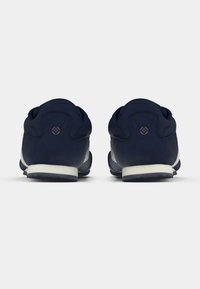 Αθλητικά παπούτσια σε ναυτικό μπλε με λείο δερμάτινο επάνω μέρος, λευκή σόλα και μινιμαλιστικό σχέδιο. Περιλαμβάνει διακριτικές λεπτομέρειες με λογότυπο στη φτέρνα.