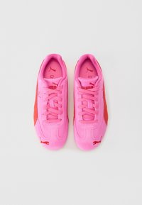 Pár jasně růžových tenisek Puma s červenými detaily a tkaničkami, zobrazených shora na jednoduchém bílém pozadí.