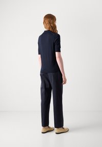 Polo cu mânecă scurtă de culoare bleumarin, cu o textură netedă, asortat cu pantaloni închiși la culoare și încălțăminte bej. Design simplu cu un guler clasic.