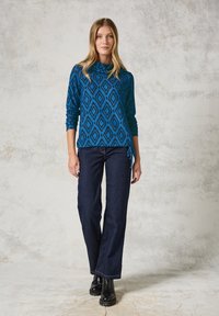Blauwe geblokte trui met diamantpatronen, gecombineerd met donkere, wijde jeans en zwarte enkelboots. Zacht materiaal met een relaxed fit.