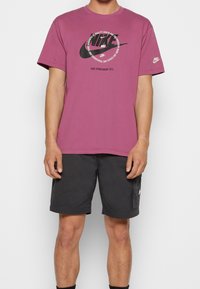 Mörkröd Nike t-shirt med korta ärmar, med en grafisk logotypdesign i svart och vitt. Bärs med svarta shorts och svarta strumpor.