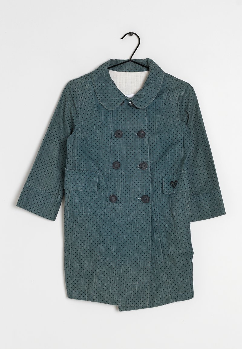 Abrigo teal de doble botonadura con lunares negros, diseño con cuello, dos bolsillos frontales y cuatro botones negros. Cuelga de un gancho negro.