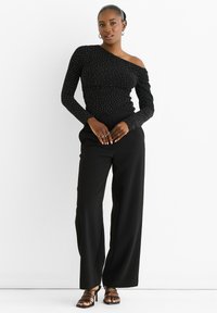Black one-shoulder top with silver embellishments, textured fabric. Paired with wide-legged black trousers and strappy black heels.