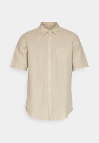 Chemise beige à manches courtes en lin, avec un devant à boutons, un col pointu et une poche poitrine unique. Texture subtile sur l'ensemble.