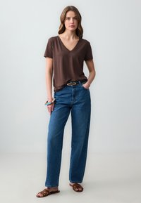 T-shirt marrone a maniche corte con scollo a V abbinato a jeans blu a vita alta e gamba dritta. Accessoriato con una cintura e sandali scivolati.
