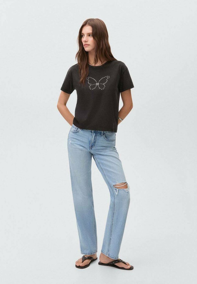 Camiseta negra con un diseño de mariposa hecha de tela suave, combinada con unos jeans desgastados de color azul claro y chanclas negras.