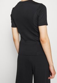 Černé sportovní tričko s krátkým rukávem, hladkou texturou, kulatým výstřihem a bezešvým designem, zobrazené zezadu s viditelnými švy.