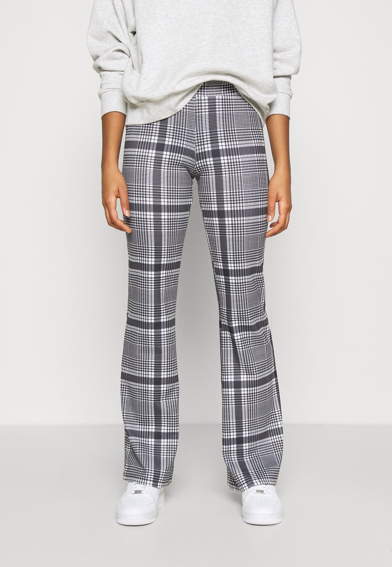 Pantalons à carreaux taille haute avec des motifs en noir et blanc et des jambes évasées, fabriqués dans un tissu confortable ; portés avec un sweatshirt gris.