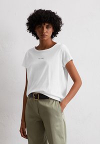 Witte katoenen t-shirt met een ronde halslijn, korte mouwen en een klein zwart logo op de voorkant, gecombineerd met olijfgroene broek.
