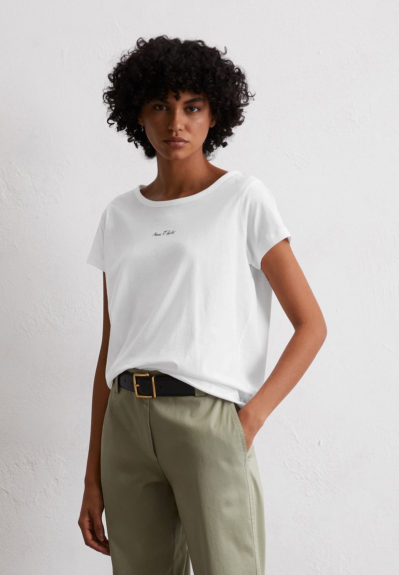 Witte katoenen t-shirt met een ronde halslijn, korte mouwen en een klein zwart logo op de voorkant, gecombineerd met olijfgroene broek.