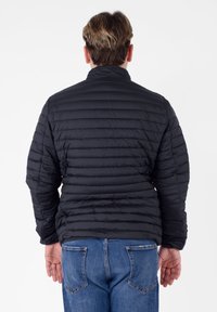 Zwarte donsjack met gestikt ontwerp, hoge kraag en textuurafwerking, gecombineerd met blauwe spijkerbroek. Zicht vanaf de achterkant.