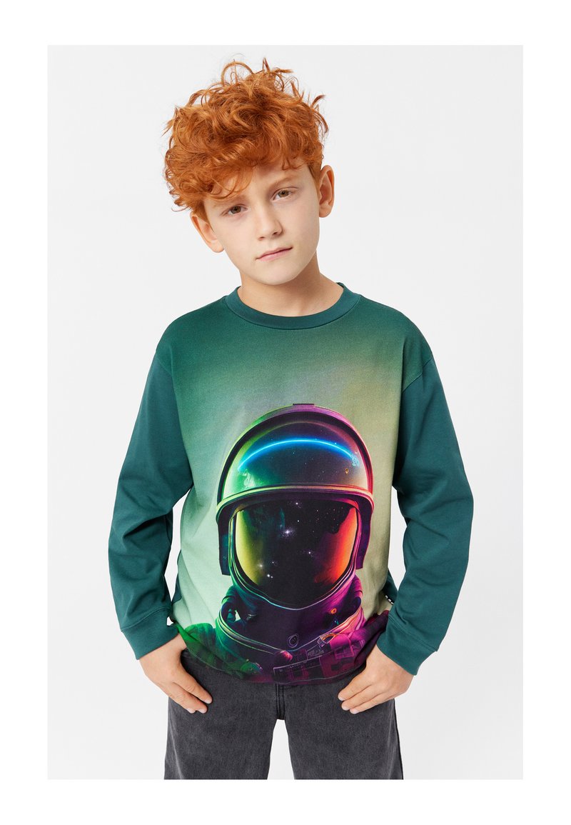 Langarmhemd in Grün mit einem Farbverlauf-Design, das eine farbenfrohe Astronautengrafik auf der Vorderseite zeigt. Aus Baumwollmaterial, lockerer Schnitt.