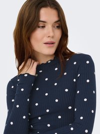 Marineblå ribbet bluse med lange ærmer, prydet med hvide prikker og en bølget halsudskæring, lavet af blødt, elastisk stof.