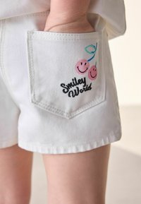 Bijele traperice kratke hlače s stražnjim džepom s ružičastim vezom trešanja i crnim natpisom "Smiley World".