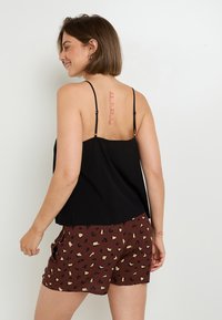 Top nero senza maniche con spalline sottili, abbinato a pantaloni corti marroni con stampa leopardata in nero e beige, indossato di lato.