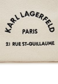 Crèmekleurige pluche stof met zwart geborduurde tekst. De tekst luidt "KARL LAGERFELD PARIS 21 RUE ST-GUILLAUME" in een ronde opstelling.