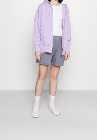 Fialová mikina na zip, bílý tričko, šedé kraťasy a bílé vysoké tenisky s akcenty. Má pohodlný design a měkké materiály.