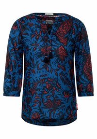 Blouse à manches longues en tissu bleu avec un motif floral en rouge et noir, dotée d'un décolleté en encoche et d'un détail de pompons à l'avant.