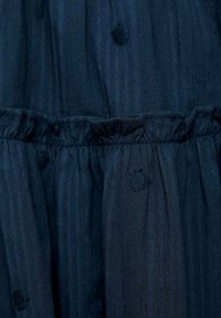 Navyblauwe stof met verticale strepen, met cirkelvormige textuuraccenten. Rimpelband met geplooide details. Gladde textuur.