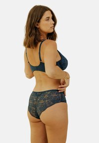 Ensemble soutien-gorge et culotte en dentelle dans un bleu sarcelle profond, avec des motifs floraux, des bretelles ajustables et une ceinture lisse avec une texture douce.