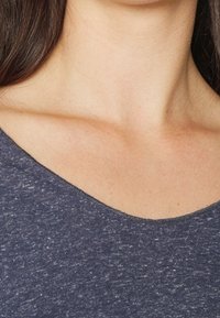 Námořnická modrá, krátkosrstá halenka s kulatým výstřihem a texturovanou tkaninou, viditelné švy po okraji, zdůrazňující neformální design.