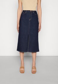 Mörkblå denim midikjol med frontslits och kontrasterande gula sömmar. Kombinerad med tanfärgade remsandaler.