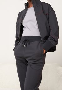 Dark gray tracksuit featuring a zip-up jacket with red stitching and a light gray t-shirt. The pants have an elastic waistband and pockets.