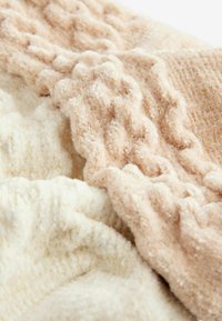 Mjuka, texturerade filtar i beige och krämfärgad med vågiga ränder och subtila glittrande detaljer, som framhäver fluffiga, mysiga material.