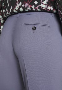 Slim-fit, světle fialové kalhoty s texturovanou látkou a zadní kapsou se černým knoflíkem detail.