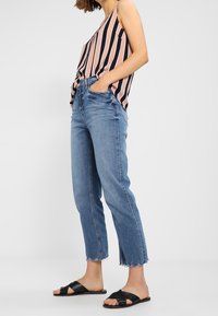 Canottiera leggera a righe in rosa e blu navy, abbinata a jeans blu con orlo sfrangiato. Il modello indossa sandali neri. Design casual e aderente.