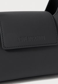 Black leather crossbody bag with flap closure and embossed "LOVE MOSCHINO" logo. Features stitched edges and a smooth texture.