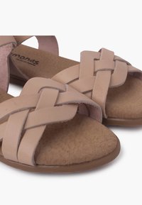 Beige nahka-sandaalit, joissa on kudotut hihnat ja pehmeä, tekstuuri-inen pohja. Pohja on tasainen, pyöreämuotoinen ja sileä.