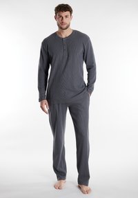 Set di pigiama grigio composto da una maglietta a maniche lunghe con una pattina a tre bottoni e pantaloni dritti abbinati, realizzati in un tessuto a maglia testurizzata.