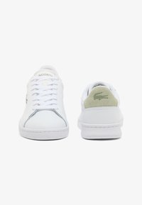 Sneakers bianche in pelle con finitura liscia, caratterizzate da un tallone in suede verde, lacci e un logo discreto sul lato. Suola spessa in gomma.