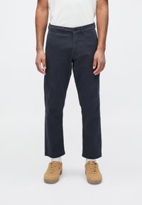 Dark navy cotton trousers with a straight cut, five-pocket design, and a button closure. Pairing with tan sneakers and white socks.