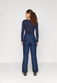 Tengerészeti sínadrág, állítható derékrésszel, két hátsó zsebbel és enyhén bővülő lábszárral, időjárásálló anyagból készült.