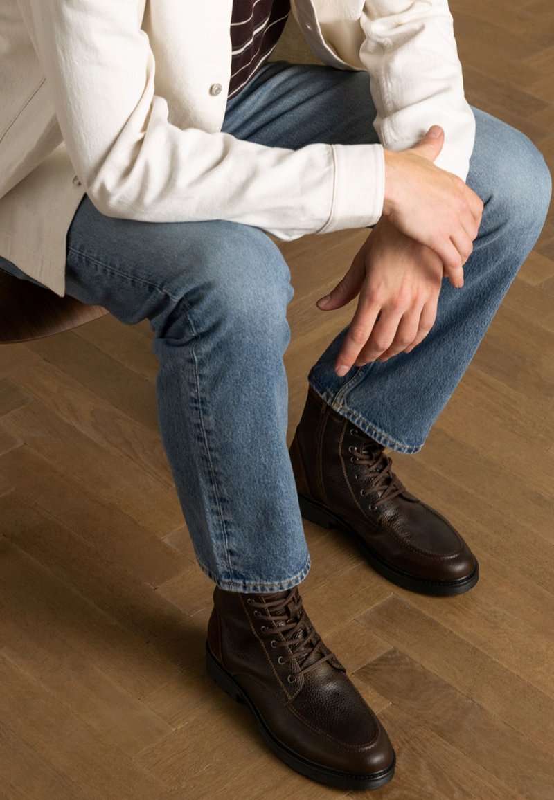 Bruine leren veterschoenen met een gestructureerde afwerking, voorzien van een stevige zool en metalen oogjes. Draag ze met een lichte spijkerbroek en een beige jas.