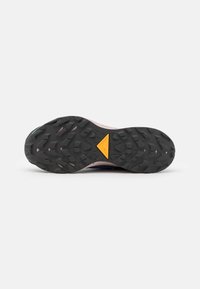 Trail løbesko med dybstruktureret sort gummi sål for greb, der har et fremtrædende gult trekantet design og en lyserød mellemsål.