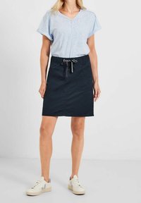 Top azul claro de manga corta con un patrón texturizado; falda negra con cordón y bolsillos; llevada con zapatillas de deporte color blanco roto.