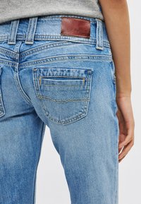 Svetlomodré riflové nohavice majú koženú nášivku na zadnej časti pásu, dve zadné vrecká so švovými detailmi a rovný strih nohavíc.