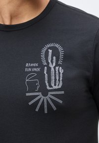 Μαύρο μπλουζάκι με λευκό γραφικό ενός κάκτου, αφηρημένη ηλιακή ακτίνα, ανθρώπινο προφίλ και κείμενο "Roark Run Amok" στο στήθος.