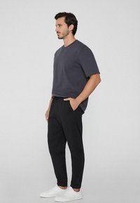 Camiseta de manga corta en gris oscuro combinada con pantalones jogger negros con cinturilla elástica y bolsillos laterales, complementada con zapatillas blancas.