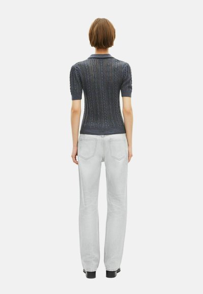 Osoba stojąca tyłem, ubrana w ciemnoniebieski krótkoszmatkowy sweter z kołnierzykiem i jasnoszare dżinsy o prostym kroju.