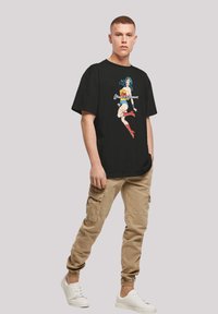 Black cotton t-shirt featuring a colorful Wonder Woman graphic on the front. The model pairs it with beige cargo pants and white sneakers.