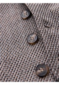 Gros plan d’un tissu texturé marron et beige avec quatre boutons cousus, trois visibles, chacun gravé avec le mot "OMBRE."
