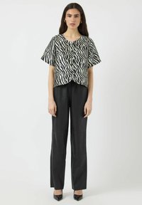 Sort-hvid zebra print kortærmet top med rund halsudskæring, parret med højtaljede sorte læderbukser og spidse sorte sko.
